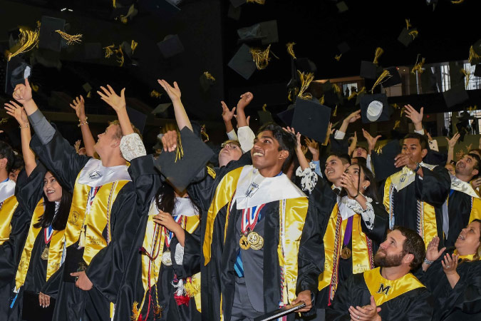 Students dressed in graduation gowns toss their caps in the air during a graduation for the Frisco Independent School District.