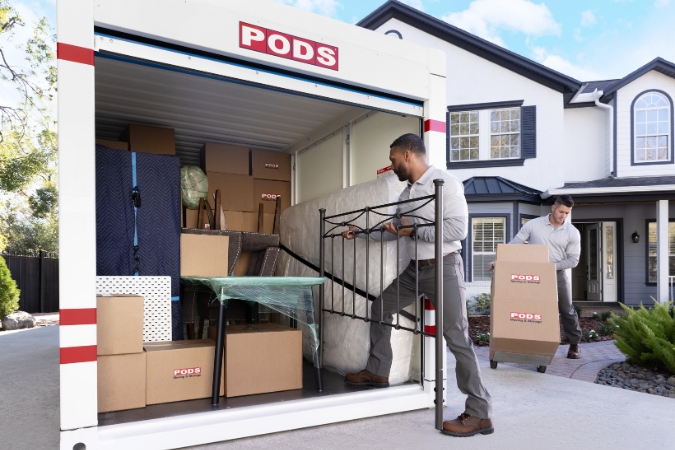 Two movers load a PODS portable storage container filled with furniture and moving boxes during a summer move.