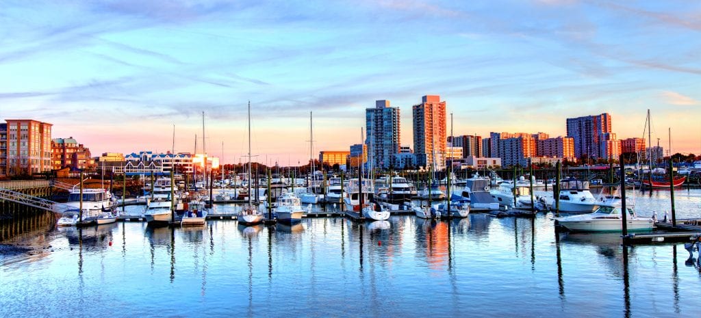 Sunset view of downtown Stamford, Connecticut — one of the NYC suburbs. Dozens of sailboats are docked on the still waters as the downtown buildings in the distance reflect pink hues from the sunset.