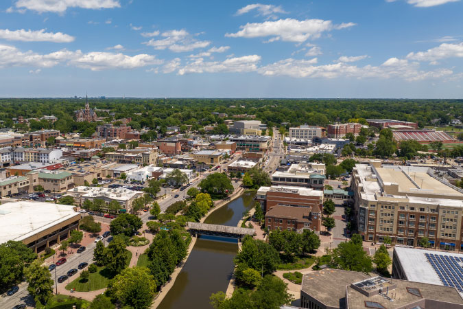 Aerial view of Naperville — one of the safest places to live in the Chicago area — featuring downtown buildings, a riverwalk, residential neighborhoods, and lots of greenery.