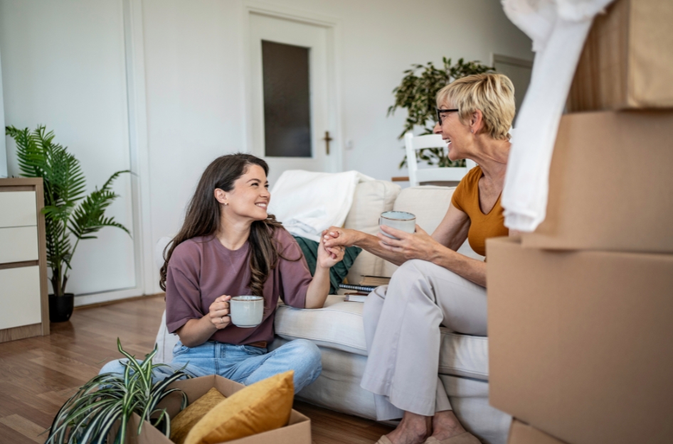 A young woman is having coffee with her mother in the living room of her family home after moving home after college.