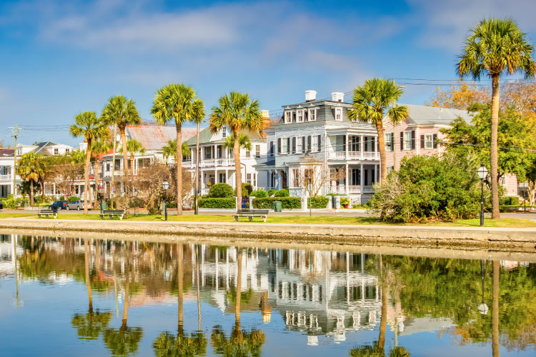 A row of traditional waterfront homes in Old Town, Charleston, South Carolina. The homes are large, with covered porches and tall palm trees in the front yards. 
