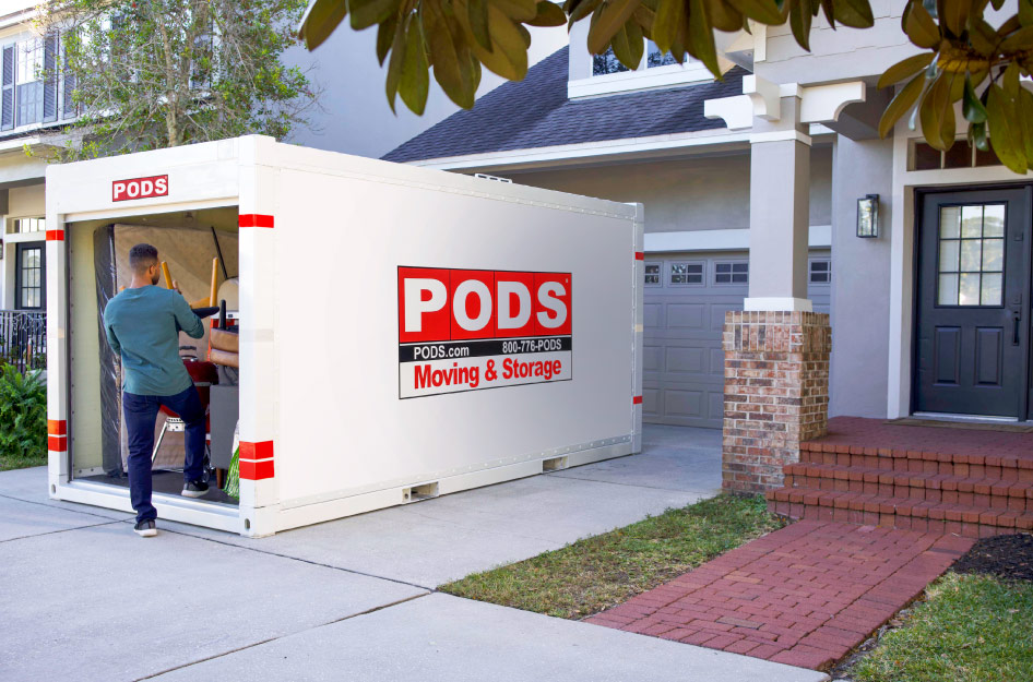 A man is unloading a chair from the PODS portable moving and storage container in his driveway.