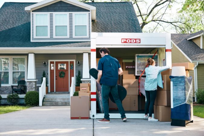 A couple is unpacking their PODS moving container filled with moving boxes that they've just had delivered to their new home.