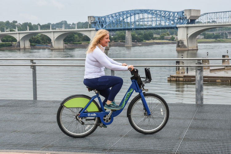 A woman is riding a rental bike from Bike Chattanooga across a bridge in Chattanooga, Tennessee.