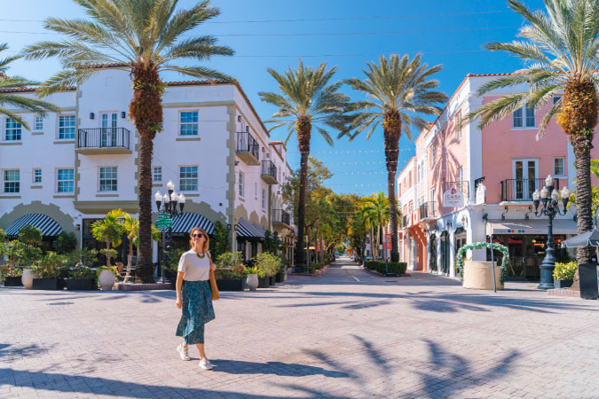 A woman in a blue skirt and white shirt is walking along a pedestrian path in South Florida’s Miami Beach, surrounded by hotels and palm trees.