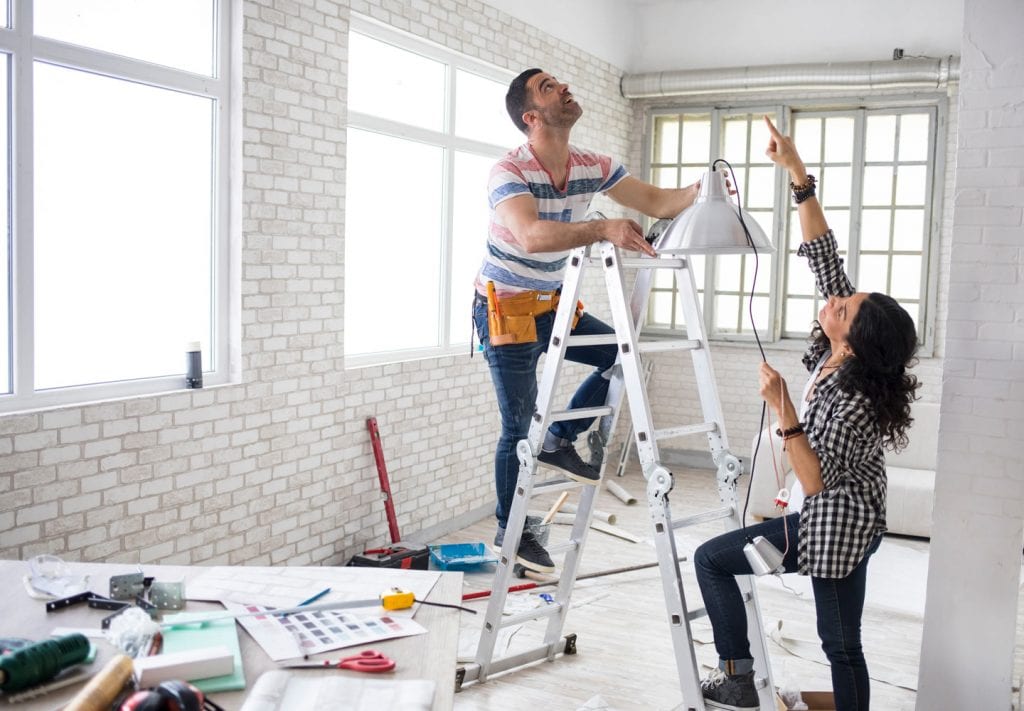 A couple installs new overhead lighting in a brick-lined apartment