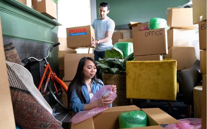 A young couple is packing up their home, surrounded by cardboard boxes