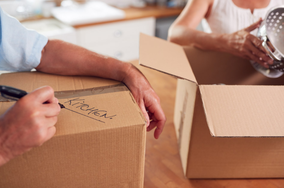 Close-up of a senior couple packing up and labeling moving boxes in their kitchen.