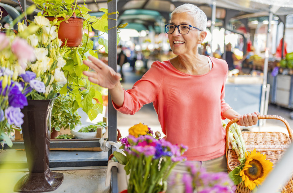 A retired woman is reaching for some fresh flowers while shopping at a farmer’s market in Michigan.