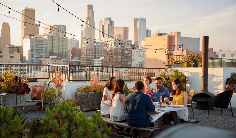 After finding an apartment in Los Angeles, a group of friends share a rooftop meal at sunset, with a view of the city skyline in the distance