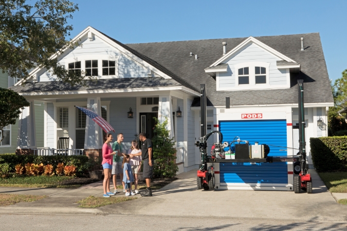 A family of four that is relocating to Little Rock, Arkansas, is talking with a PODS driver in their driveway in the middle of receiving a PODS container delivery.