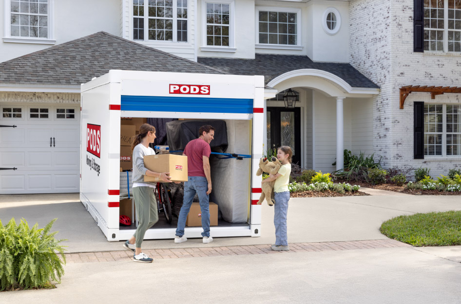 A family of three loads a PODS moving and storage container in their driveway after deciding to move with PODS vs. U-Pack.