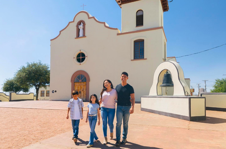 A family of four is walking in front of an adobe church in El Paso, Texas, on a sunny day.