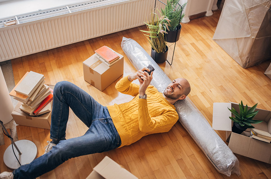 A man reads his phone, laying on a rolled-up carpet.
