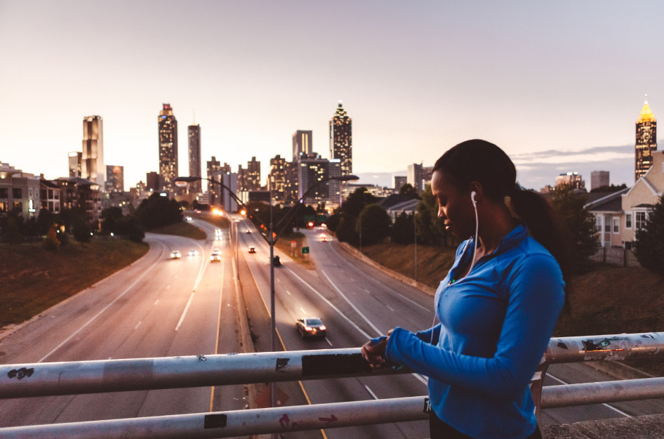 A woman is pausing from her run on an overpass in Atlanta, Georgia, with the city skyline visible in the distance