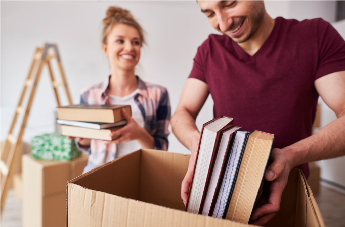 A young couple is assessing how to pack books for moving while loading their moving boxes.