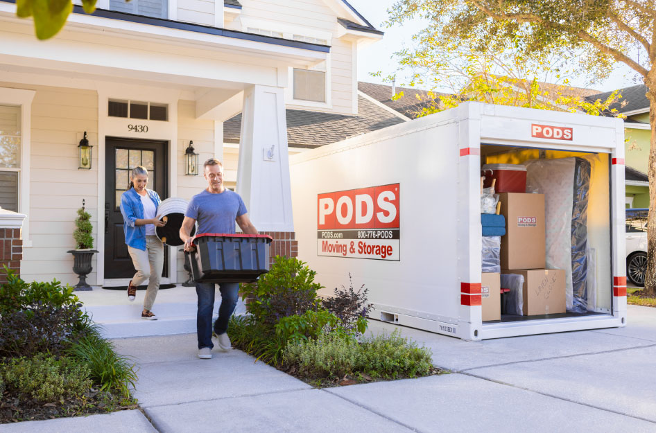 A mature couple is loading items into the PODS portable moving container in their driveway, showcasing PODS local moving services.