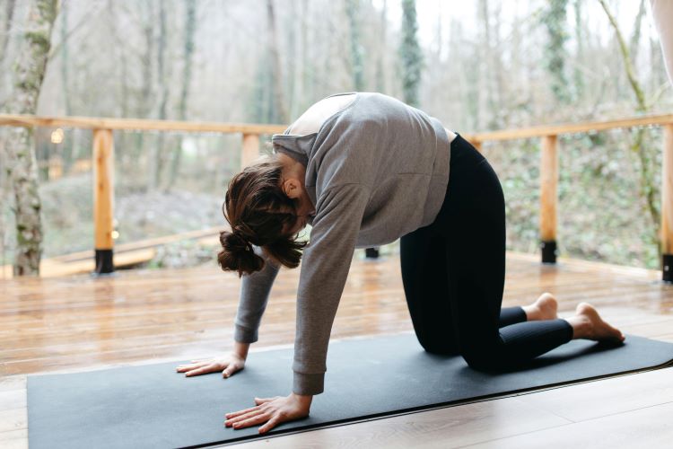 A woman in a grey sweatshirt practices the cat-cow yoga move as a way to reduce stress during her move.