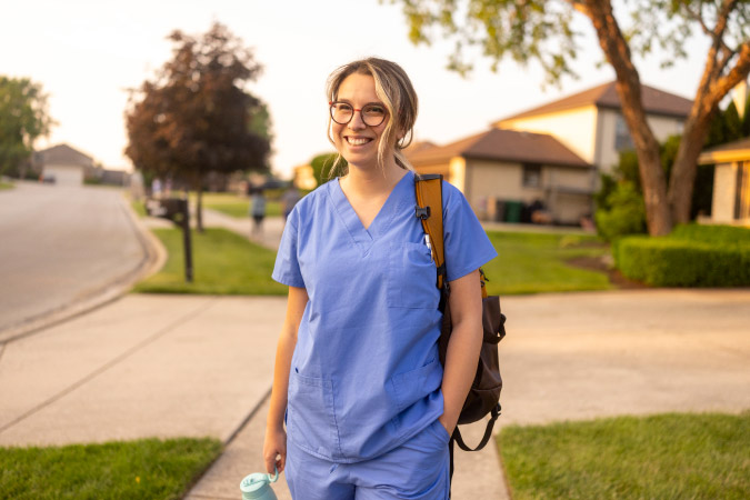 A young nurse is standing in the sunshine, smiling, as she prepares to go to work for the day.