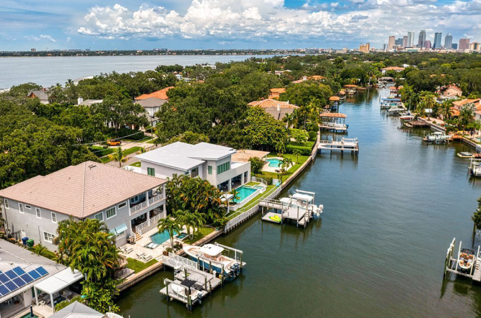 Aerial view of the Davis Islands neighborhood of Tampa, Florida. Luxury waterfront mansions dot the waterway, each with its own private dock. In the distance, Tampa’s skyline can be seen against a cloudy blue sky.