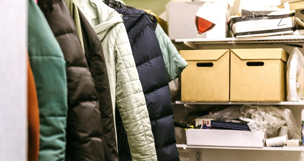 View inside a closet that is filled with jackets and boxed-up knick-knacks.