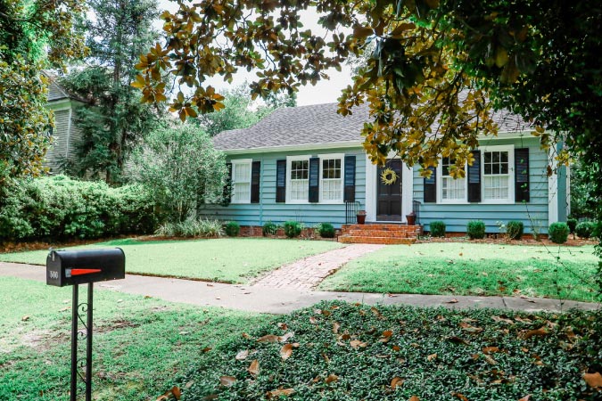 A small cottage-style home with a simple lawn, surrounded by lush foliage — similar to homes you’d find in some of the nicest neighborhoods in Baton Rouge.