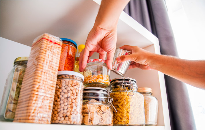 Close-up of a pair of hands taking a couple of items out from a pantry shelf.