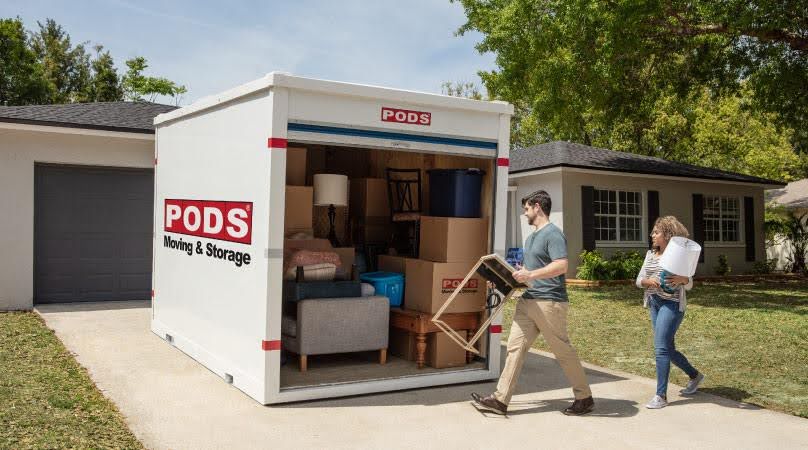 A man and woman are loading a PODS portable moving container in their driveway as they prepare for moving to Charleston, SC.