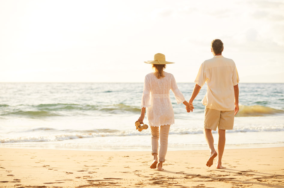 A retired couple is walking hand-in-hand on a beach in Savannah, GA, just before sunset.