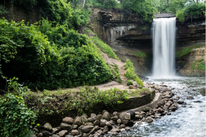 Minnehaha Falls cascades into a rocky stream surrounded by lush greenery in Minnesota, considered by some to be the best state to buy a house.