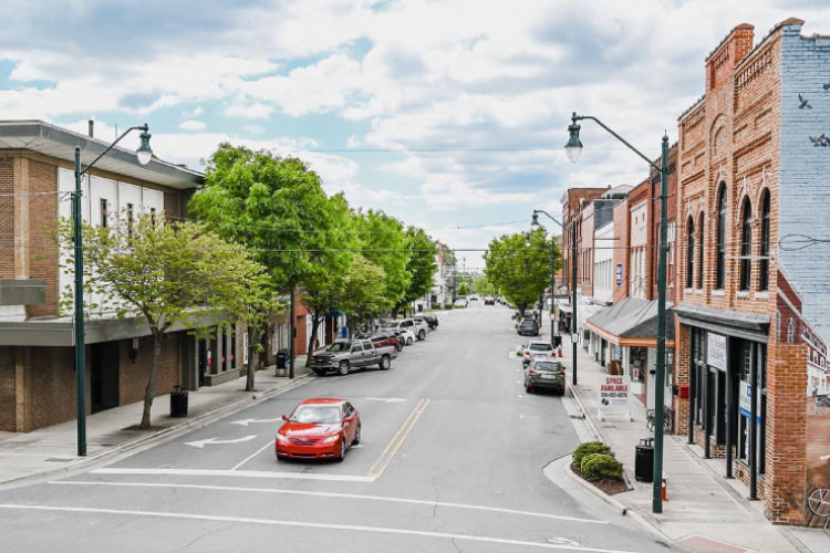 Rooftop view of Downtown Asheboro, North Carolina, on a clear summer day. The downtown buildings are relatively short, and all appear to be made of red brick. Lush trees line the streets, and cars are parked along the sidewalks.