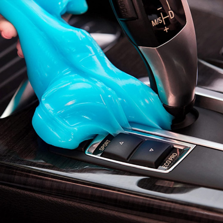 Close-up view of a hand using blue slime to pick up dirt and debris from a car’s center console.