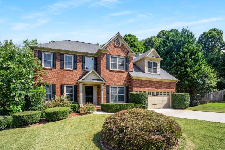 A beautiful, two-story brick home with a manicured lawn is nestled among a lush wooded grove in Marietta, Georgia.