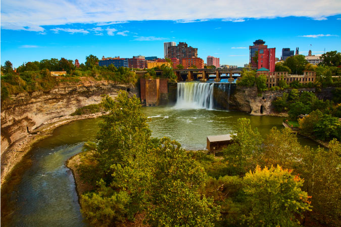 Distant view of the skyline of Rochester, New York, with a river and waterfall in the foreground