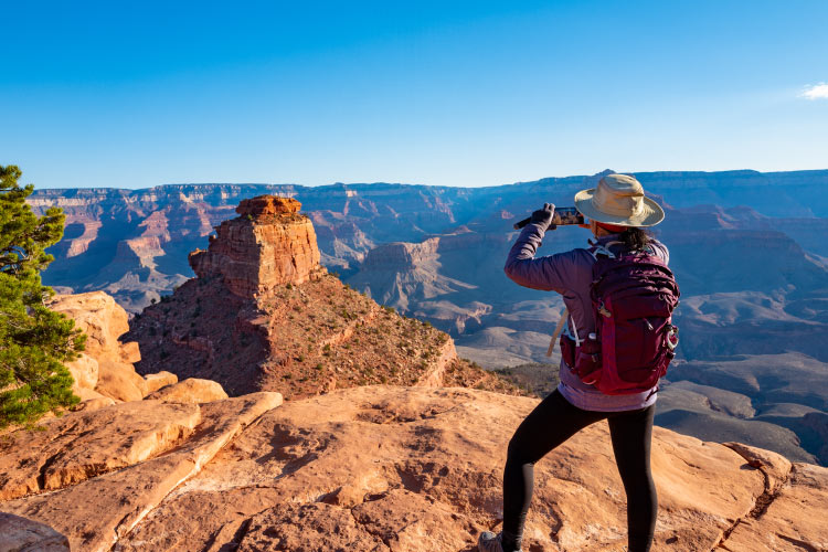 A woman in hiking gear is taking a photo of the Grand Canyon from the South Rim, thoroughly enjoying retirement in Arizona.