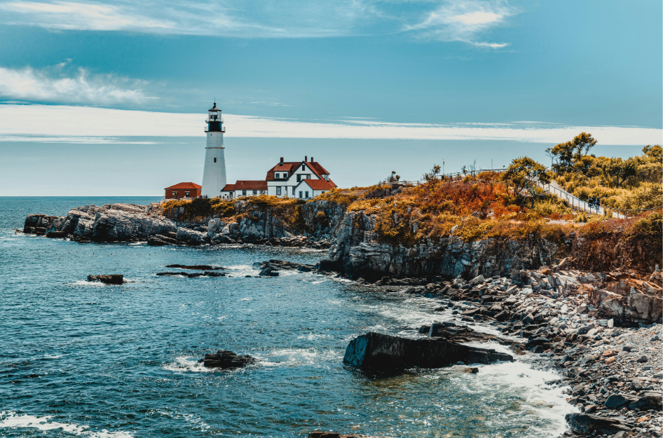 A view of Cape Elizabeth, ME, with a lighthouse and a lighthouse keeper's home. Views like this are a perk of retiring in Maine.