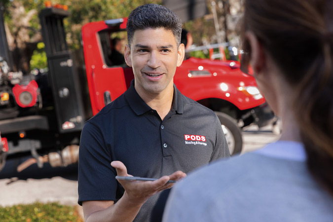View over a woman’s shoulder as she speaks with a friendly PODS driver about PODS moving costs, with his red truck visible in the background.