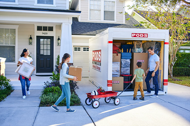 A family (mom, dad, a young boy and girl), pack their fully loaded PODS container. 