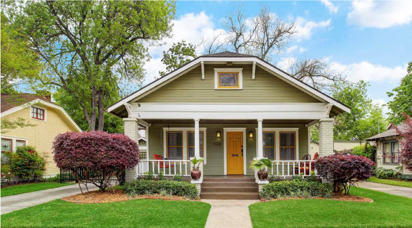 A lovely historic bungalow with a covered porch and a yellow door in The Heights neighborhood of Houston.