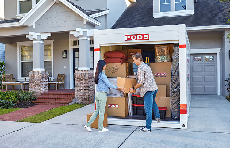 A husband and wife load their PODS container in their driveway