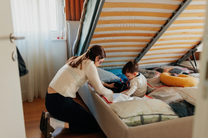 A young mother and her son are organizing items in the vast storage space under a bed, one of many bedroom organization hacks to keep a bedroom in good order.