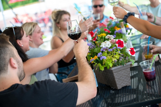Friends toasting with wine at an outdoor table decorated with colorful flowers at Black River Farms, highlighting one of the many things to do in Bethlehem, PA.