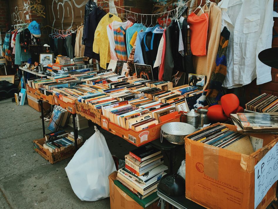 Clothes on racks and rows of books in boxes are staged for a garage sale.