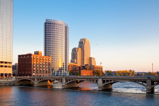 View of Grand Rapids, Michigan, with tall city buildings on the waterfront and a bridge spanning the Grand River.