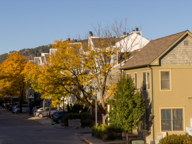 A residential street accommodating residents living in Boulder, CO, and featuring two-story homes and mature trees with fall foliage.
