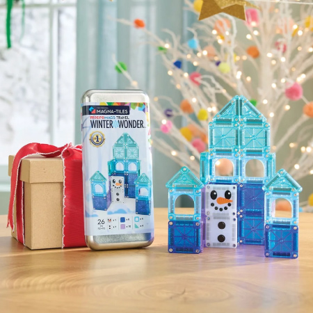 A blue castle made of MagnaTiles — a perfect example of kid-friendly white elephant gifts —is set up beside the tin it came in and a holiday gift box.