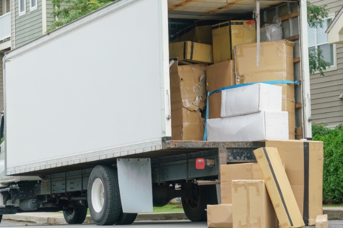 A moving truck is parked outside a suburban home, almost fully loaded with moving boxes in preparation for a long-distance move.