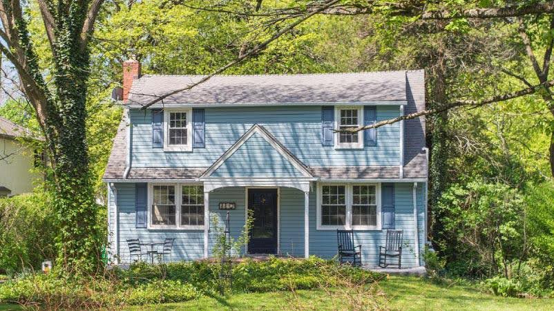 A blue, two-story residential home in Devon, Pennsylvania — one of the towns outside of Philadelphia — surrounded by vine-covered trees and a wild green lawn.