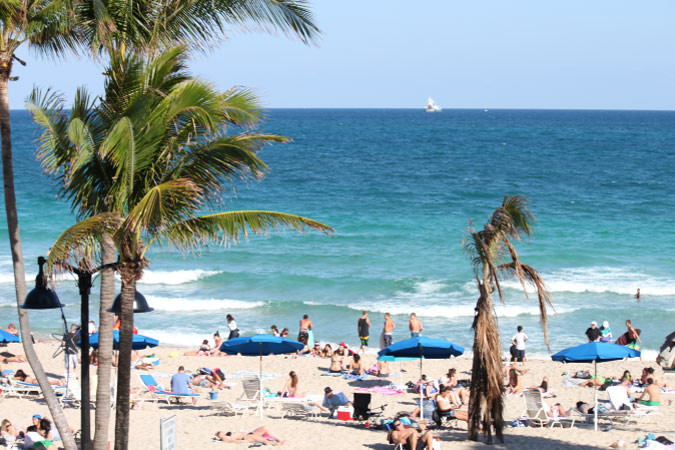 Beachgoers enjoy a sunny day at Florida’s Fort Lauderdale Beach, with blue waters, sugar sand, and shady palm trees.